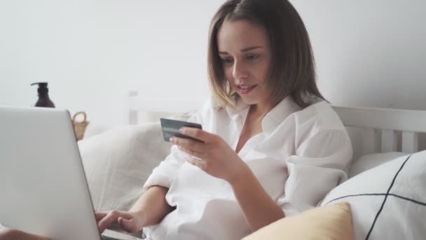 Mujer compra en línea en casa. chica introduce el número de tarjeta de crédito en el ordenador portátil. compras adictas a las compras en Internet — Vídeo de stock