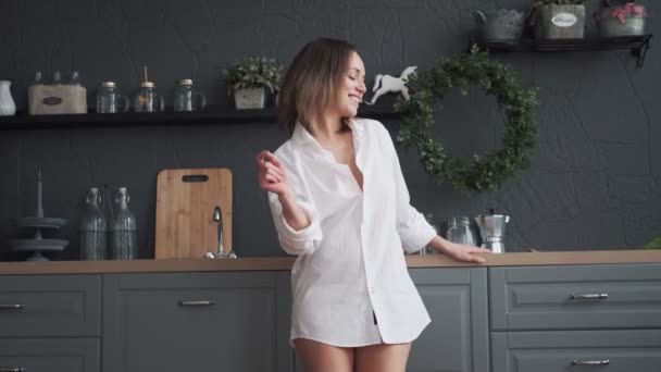 Lycklig kvinna bekymmerslös dans i köket tidigt på morgonen. flicka dansar roligt och ler — Stockvideo