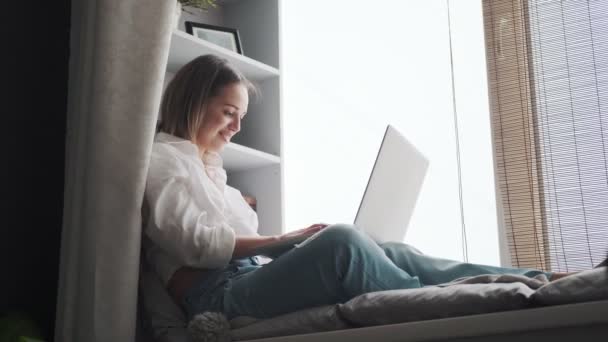 Giovane donna lavora su un computer portatile sullo sfondo di librerie. ragazza con un computer portatile ride e ride — Video Stock