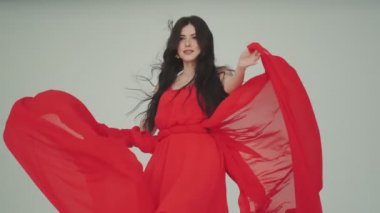 Kırmızı elbiseli genç bir kadın. Kumaş rüzgarda sallanıyor. Reklam parfümleri ya da diğer kavramlar için modaya uygun bir görüntü.