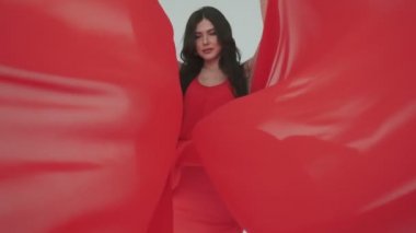 Rüzgarda çırpınan kırmızı elbiseli parlak genç bir kadının portresi. Kumaş rüzgarda sallanıyor. Reklam parfümleri ya da diğer kavramlar için modaya uygun bir görüntü.