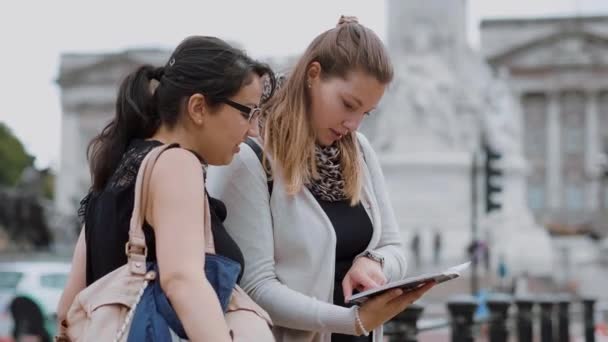 Dos mujeres jóvenes leen en una guía de viaje durante un viaje a la ciudad — Vídeos de Stock