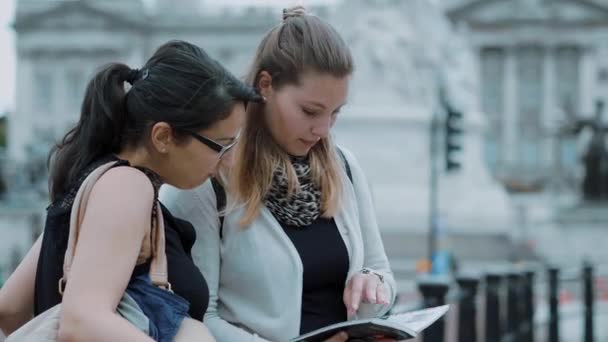 Duas jovens mulheres lêem em um guia de viagem durante uma viagem à cidade — Vídeo de Stock