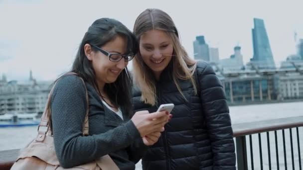 Две девушки смотрят фотографии на мобильном телефоне — стоковое видео