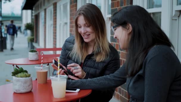 Две молодые женщины сидят в уличном кафе и отдыхают — стоковое видео
