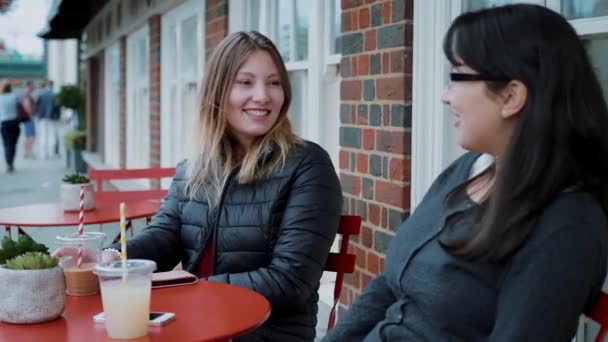 Две молодые женщины сидят в уличном кафе и отдыхают — стоковое видео
