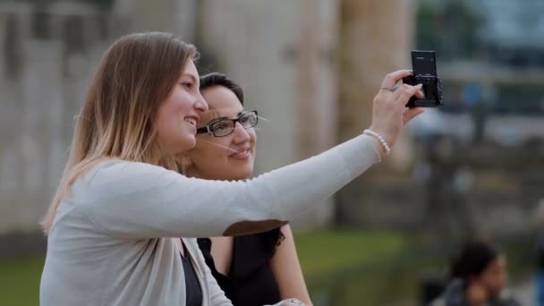 Dos jóvenes amigos se toman selfies mientras están sentados en una pared — Vídeos de Stock