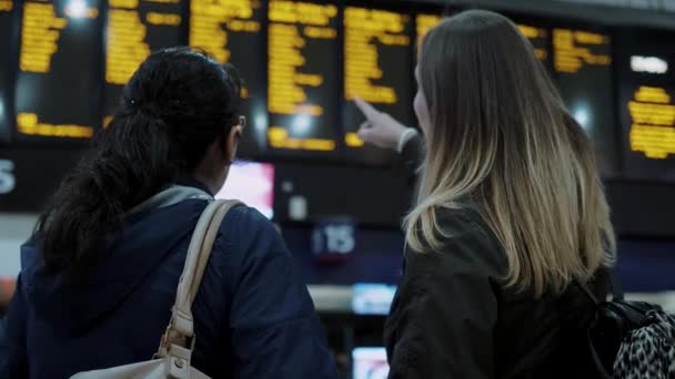 Zwei Mädchen kontrollieren den Abreisetisch an einem Bahnhof — Stockvideo