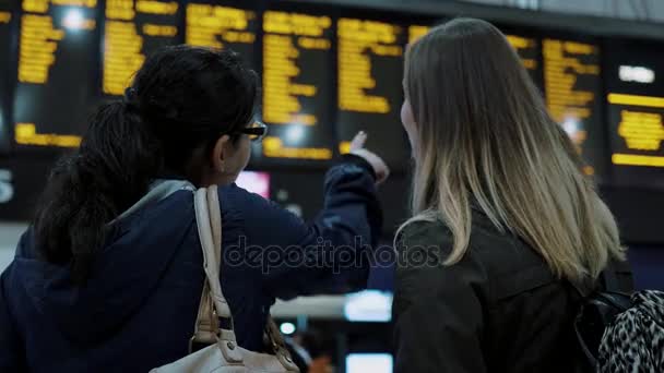 Zwei Mädchen kontrollieren den Abreisetisch an einem Bahnhof — Stockvideo