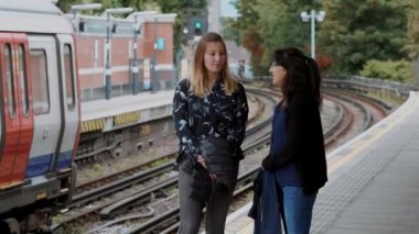 İki genç kadın Londra metro istasyonunda metro bekleyin