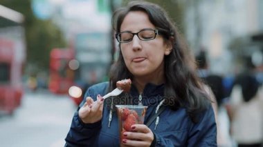 Genç kadın taze çilek Londra sokaklarında yiyor.