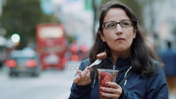 Молодая женщина ест свежую клубнику на улицах Лондона — стоковое видео