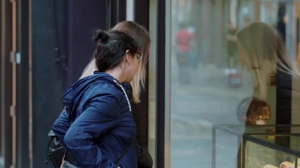 Дві дівчини дивляться вікна магазину на торговій милі — стокове відео
