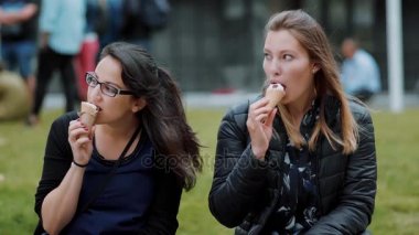 İki kız bir parkta çayırlar üzerinde oturup dondurma yemek