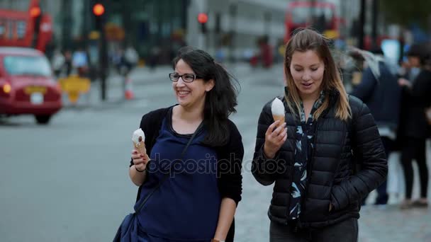 Две молодые женщины ходят по Лондону с мороженым в замедленной съемке — стоковое видео