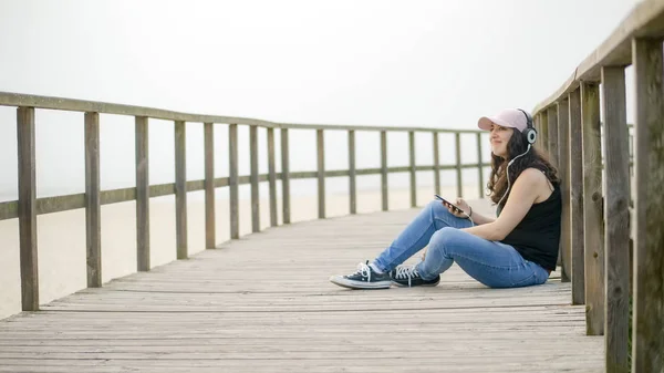 Jovem mulher senta-se em um cais de madeira na praia — Fotografia de Stock