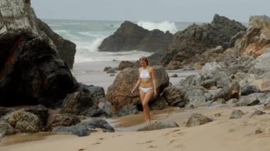 Fırtınalı deniz arka planında kumsalda yürüyen seksi kız. Yavaş çekim görüntüleri