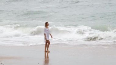 Fırtınalı deniz arka planında kumsalda yürüyen seksi kız. Yavaş çekim görüntüleri