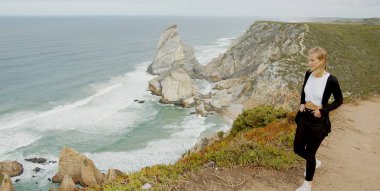 Genç bir kadın Portekiz 'deki Cabo da Roca' da okyanus manzarasının tadını çıkarıyor. Seyahat fotoğrafçılığı.