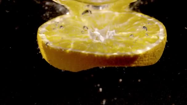 ゆっくりとした動きで水の中に落ちるオレンジのスライス — ストック動画