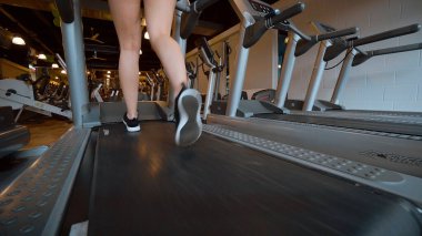 Kız spor salonunda koşu bandında koşuyor.