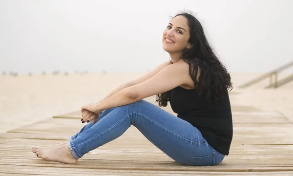 Giovane donna si siede su un molo di legno in spiaggia — Foto Stock