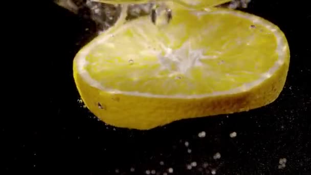 El trozo de la naranja que cae en el agua en la cámara lenta — Vídeo de stock