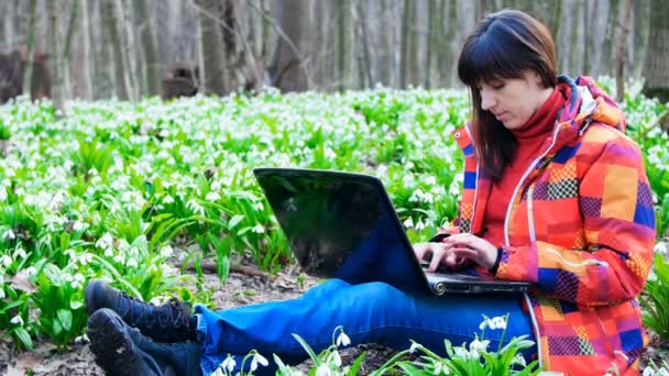 Egy gyönyörű fiatal lány dolgozik a laptop közepén a tavaszi erdő tele van virágzó hóvirág