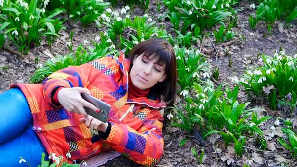 Una bella donna fa un selfie con bucaneve in fiore su uno sfondo in una foresta primaverile — Video Stock