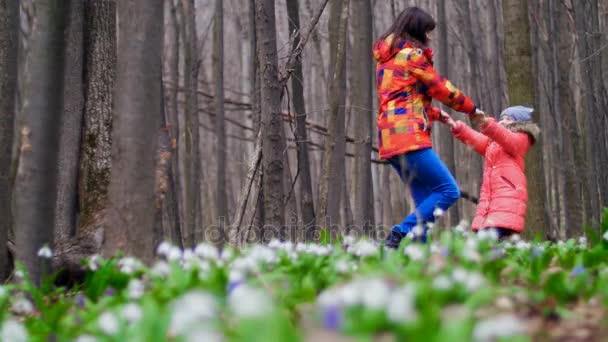 Belle mère heureuse et fille mignonne s'amuser et sauter à travers la forêt printanière pleine de gouttes de neige, dans une journée ensoleillée 