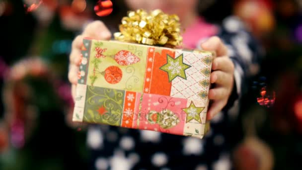 Primer plano de dos manos de niño sosteniendo un regalo de Navidad en una hermosa envoltura de papel de color con un arco de oro — Vídeos de Stock
