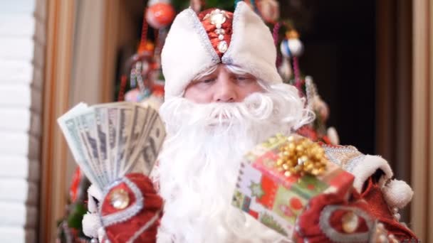 Santa claus, father christmas, father frost chooses what is better to give money dollars or a Christmas gift in a colorful paper wrapper with a gold bow as a present for Christmas or new year, in the — Stock Video
