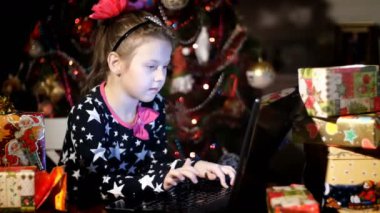 Parlak renkli kağıt paketlerinde hediyeler arasında gece alacakaranlık pembe fiyonk saç ve güzel bir elbise ile güzel sarışın kız Noel Baba, baba bir mektup yazmakta olduğunu