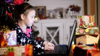 Parlak renkli kağıt paketlerinde hediyeler arasında gece alacakaranlık pembe fiyonk saç ve güzel bir elbise ile güzel sarışın kız Noel Baba, baba bir mektup yazmakta olduğunu