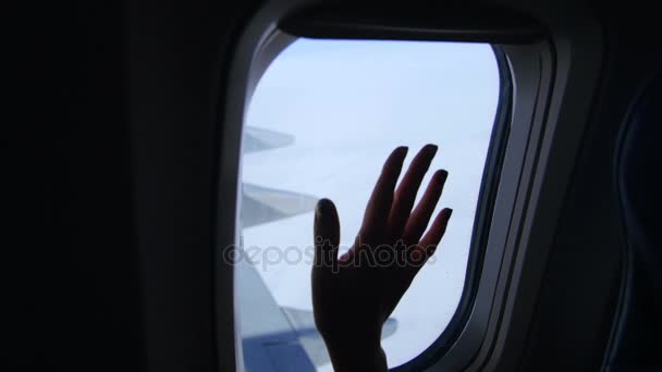 Aus dem Flugzeugfenster sieht man die dunkle Silhouette der weiblichen Hand, die Handfläche, die Bewegung der Finger, den Himmel, die Wolken, den Flügel des Flugzeugs. das Wetter ist klar, sonnig — Stockvideo