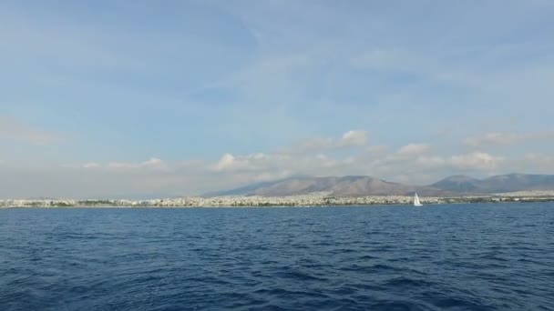 Sie können die Landschaft der Berge und des Mittelmeeres sehen, in der Ferne die Häuser von Athen, Griechenland. Sommerklarer Tag, weiße Wolken am Himmel, ruhiges Meer. Blick vom Meer — Stockvideo