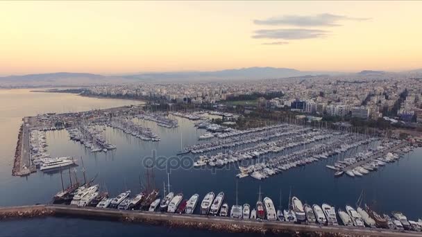 Amanecer en el puerto deportivo griego, Atenas. Grabación de video Aero. Muchos yates diferentes, catamaranes amarrados a muelles. En el fondo se encuentra el paisaje de las montañas y las casas de la ciudad. Verano claro — Vídeo de stock