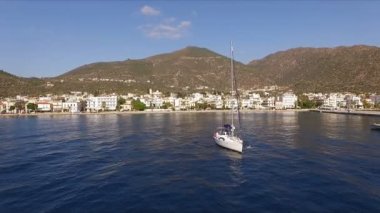 Güneşli sabah boş bir Yunan Marina, Methana, Akdeniz. Havadan video çekim, bir kuş uçuş yüksekliği. Yalnız yelkenli yat marina bırakır. Arka planda bir manzara olduğunu