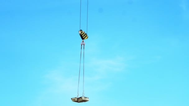 Primo piano. Contro il cielo blu, una gru da costruzione tira qualcosa, trasporta, solleva materiali da costruzione — Video Stock