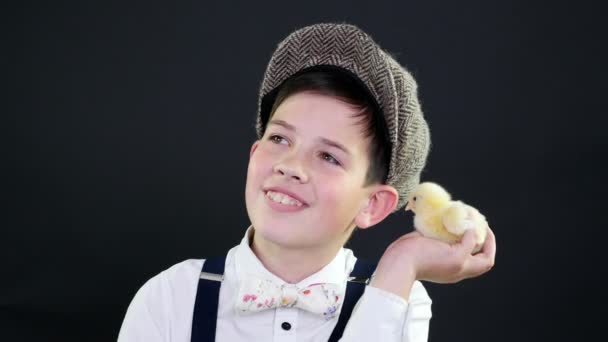 Retrato, un chico guapo con gorra y tirantes juega con un patito amarillo. Estudio de vídeo con decoración temática — Vídeos de Stock