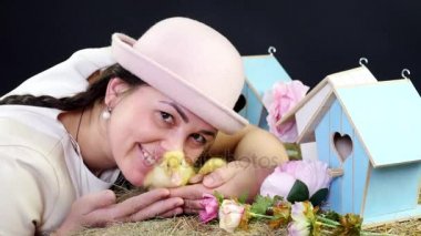Portre, genç ve güzel bir kadın ile iki kuyruklu ve küçük sarı ördek yavrusu ile oynarken komik pembe şapkalı. Stüdyo tematik dekor ile video.