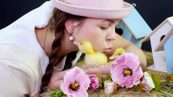 Portret, een mooie jonge vrouw met twee pigtails en in een grappige roze hoed spelen met kleine gele kuikens. Studio video met thematische inrichting. — Stockvideo