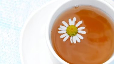 Yakın çekim, beyaz bir bardak çay, üzerinde yüzen bir papatya çiçeği ile