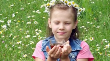 Çimenlikte papatya, papatya, çelenk içinde bir cam bardak papatya çayı içme ve çok gülümseyen tatlı bir kız