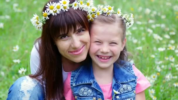Summer, amidst a chamomile lawn, in the forest, a young woman, a brunette and a girl of seven, mother and daughter weave a wreath of chamomiles, laughing, trying on wreaths — Stock Video