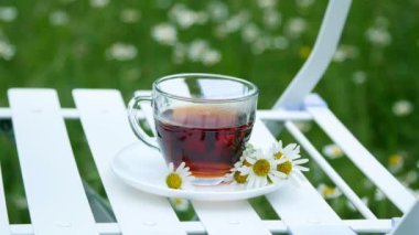 Yakın çekim, yavaşlama. Papatya ile dekore edilmiş beyaz bir daire üzerinde bir cam bardak çay ile vardır. Süt içine dökülür. Arka planda bir yeşil, papatya çayır olduğunu