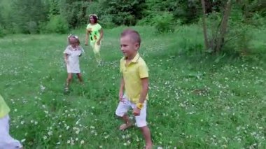Ormanın yakınında papatya çayır üzerinde topla oynayan çocuklar anneleri ile birlikte. Eğleniyorlar. Summer, açık havada, ormanda. Çocuklu tatil