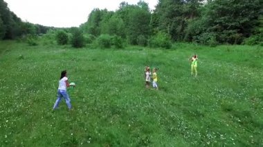 Aero, video yukarıdan çekim. Ormanın yakınında papatya çayır üzerinde topla oynayan çocuklar anneleri ile birlikte. Eğleniyorlar. Summer, açık havada, ormanda. İle tatil
