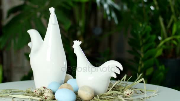 Rotation, die festliche Osterkomposition in den Lichtstrahlen, auf dem Stroh stehen zwei weiße Statuetten von Henne und Hahn. Bunte Ostereier werden ausgebreitet — Stockvideo