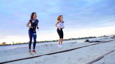 Güzel, ince genç kadın fitness içinde nişanlandık, atlama, güç egzersizleri gerçekleştirmek. Şafakta, kumlu taş ocağı plajda güneşin karşı çekim video.